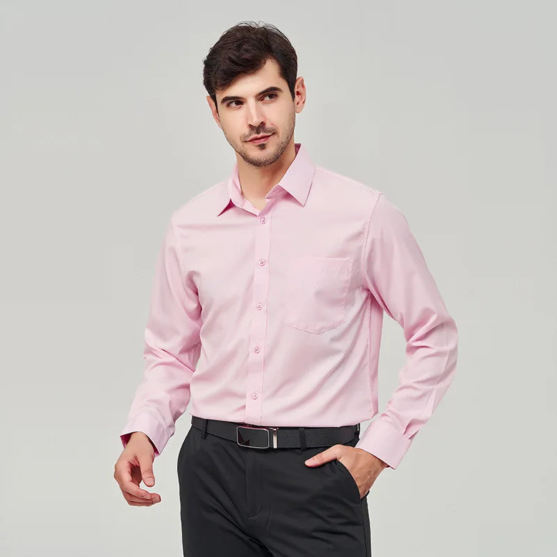 A front view of a man standing, with one hand in pocket, wearing a pink button up dress shirt, dark blue pants and a black belt.