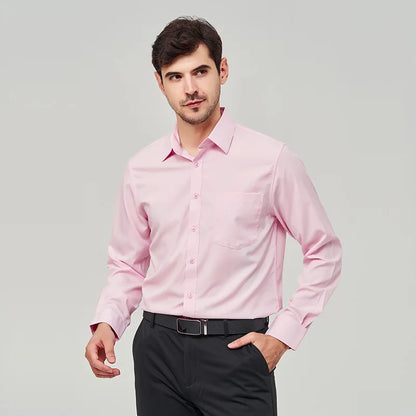 A front view of a man standing, with one hand in pocket, wearing a pink button up dress shirt, dark blue pants and a black belt.