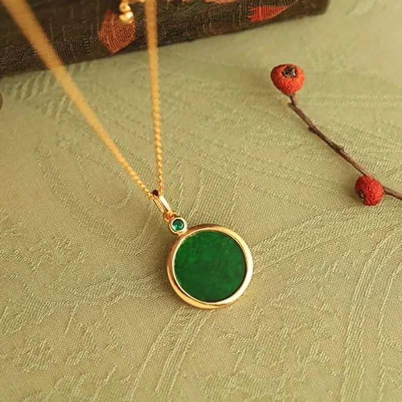 Gold necklace with a green pendant on a textured surface with red berries.