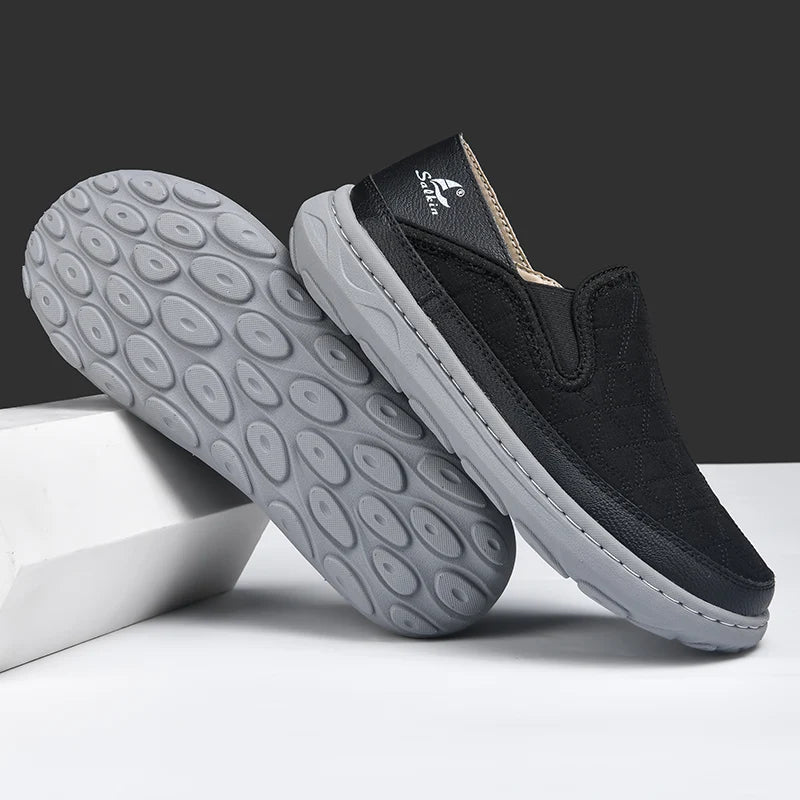 Black slip-on shoes with gray soles on a white surface