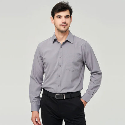 A front view of a man standing, wearing a gray button up dress shirt, dark blue pants and a black belt.
