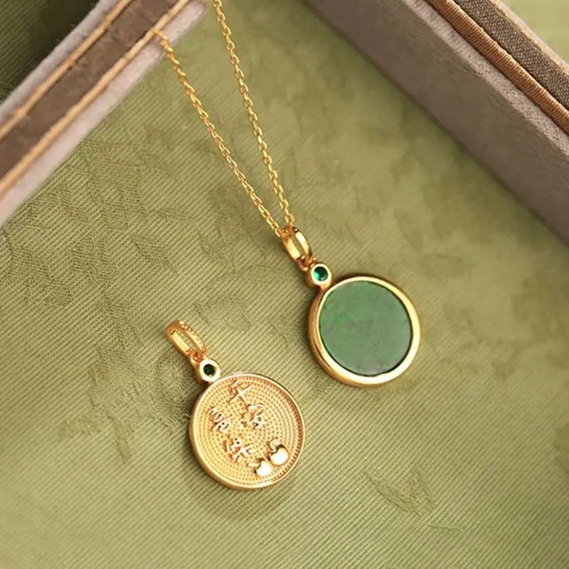 Two gold pendants on a green fabric background
