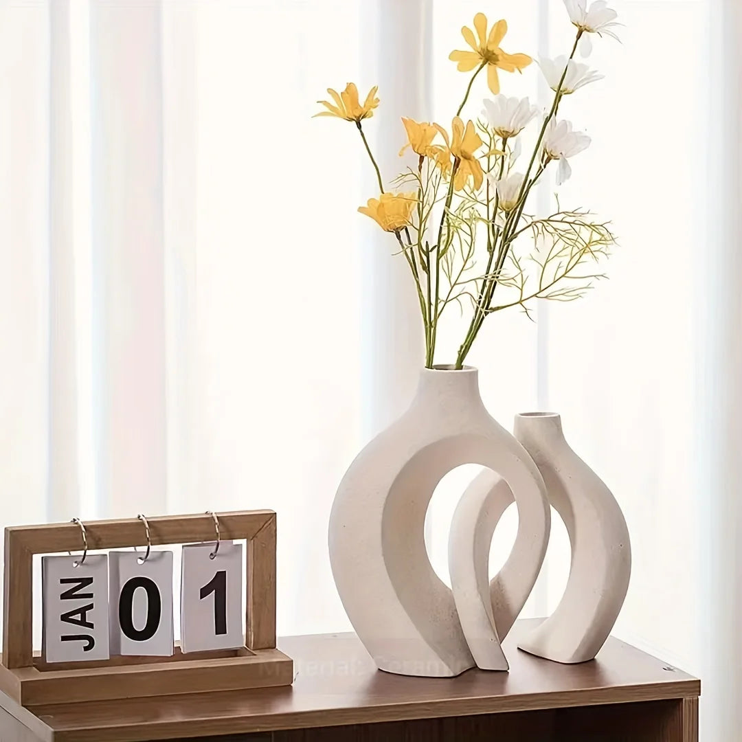 Two white ceramic vases with yellow and white flowers on a wooden surface.