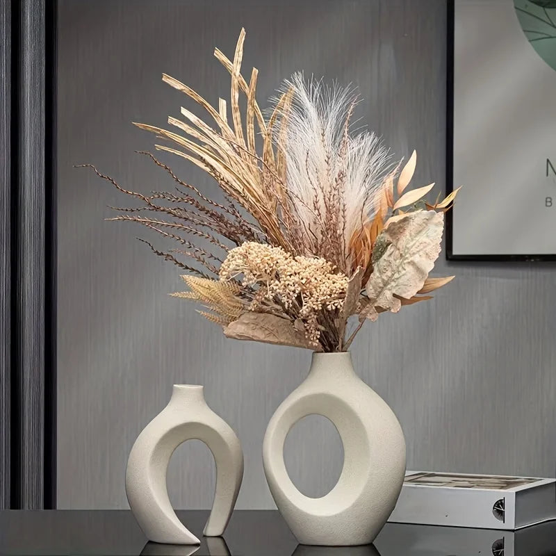Two white ceramic vases with a dried flower arrangement on a reflective surface.