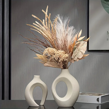Two white ceramic vases with a dried flower arrangement on a reflective surface.